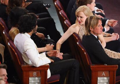 El actor Dev Patel (izquierda) es saludado por la actriz Nicole Kidman que aparece sentada junto a su esposo Keith Urban. 
