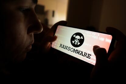 Una persona mira la pantalla de un móvil con una representación de 'ransomware'