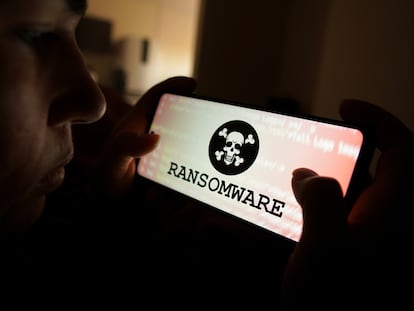 Una persona mira la pantalla de un móvil con una representación de 'ransomware'