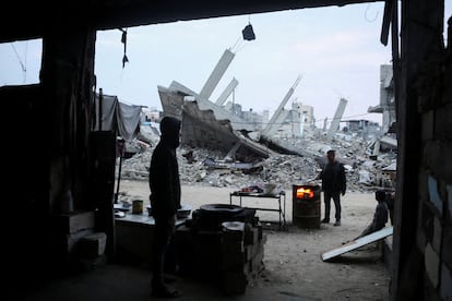 Un palestino mira mientras otro hombre cocina cerca de los escombros de edificios destruidos en anteriores ataques israelíes, este jueves en Gaza. 