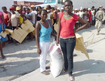 Manoucha (izquierda) y Beatriz (derecha), con sus sacos de arroz junto a la fila donde las mujeres haitianas esperan a recibir ayuda humanitaria.