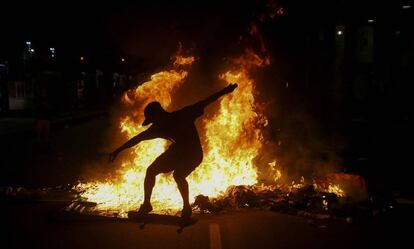 Jovem no skate em meio às chamas após a repressão policial a protesto no Rio.