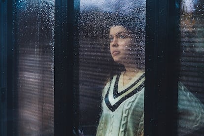 Teenage girl looking through wet window