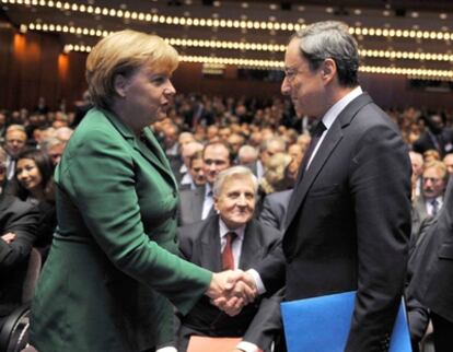 Merkel saluda al sucesor de Trichet, el italiano Mario Draghi, ante la mirada del presidente saliente del BCE.