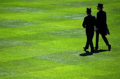 Dos asistentes a la carrera con sombreros de copa caminan sobre un césped el primer día de la Royal Ascot. 