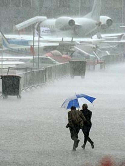 Dos visitantes recorren el Salón de Le Bourget en medio de la lluvia.