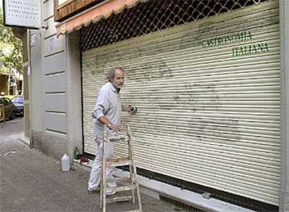 Un empleado de la limpieza borra las pintadas contra Laporta en la fachada de una tienda cercana a su domicilio.