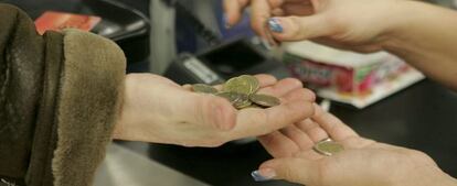 Una cajera ayuda a un cliente a contar las monedas de euro en un supermercado.