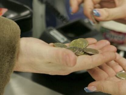 Una cajera ayuda a un cliente a contar las monedas de euro en un supermercado.