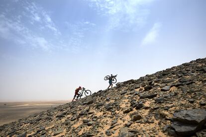 Dos ciclistas cargan con sus bicicletas durante la quinta etapa de la 13ª edición de la carrera de ciclismo de montaña Titan Desert 2018 cerca de Merzouga (Marruecos), el 3 de mayo de 2018.