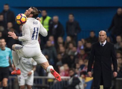 Gareth Bale (izquierda) del Real Madrid salta para golpear el balón ante la mirada de su entrenador Zinedine Zidane.