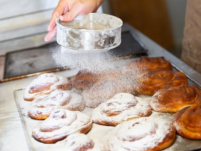 Baker hands dusting freshly baked ensaimadas with powdered sugar in bakery. Baking process of traditional Spanish pastries