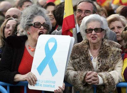 Dos mujeres muestran un cartel con el lazo azul, símbolo de la marcha convocada por el PP.