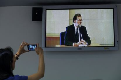 Una periodista hace una foto con su teléfomo móvil a la pantalla donde se ve al presidente del Gobierno, Mariano Rajoy, testificar como testigo en el juicio del caso Gürtel, en la Audiencia Nacional en San Fernando de Henares, el 26 de agosto.
