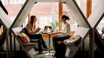 Dos chicas hablando con auriculares puestos en una mesa.