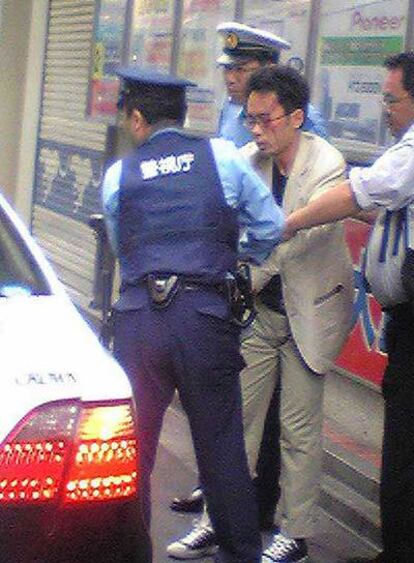 Varios policías conducen detenido a Tomohiro Kato, con traje claro.