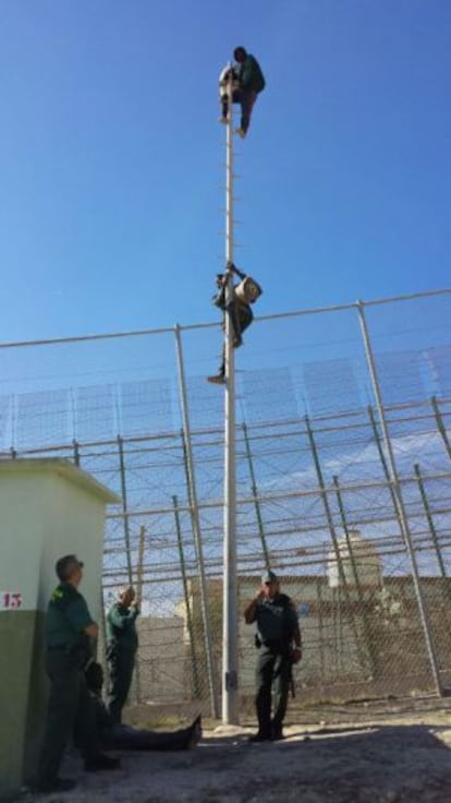 Dos inmigrantes permanecen subidos a un poste en la valla de Melilla.