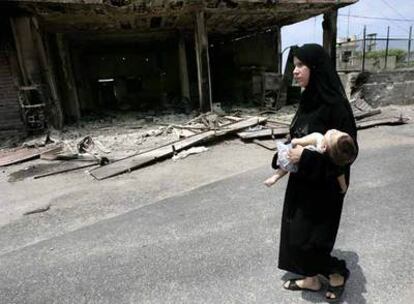 Una mujer palestina y su bebé pasan ante una gasolinera quemada en el campo de refugiados de Naher el Bared.