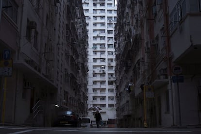 Homem caminha na frente de um edifício residencial e comercial onde se localizam casas-caixão em Hong Kong.