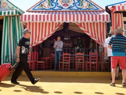 Un visitante, con su equipaje en la Feria de Sevilla mientras un grupo de turistas observa las casetas.