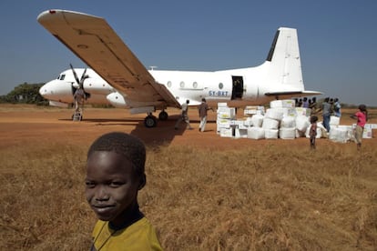 Unos niños observan a un grupo de trabajadores que descarga un contenedor lleno de vacunas de un avión en el aeropuerto de Aweil, en Sudán del Sur.