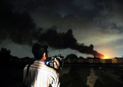 Un reportero graba las llamas y el humo que salen de la base aérea militar atacada por los talibanes en Karachi.