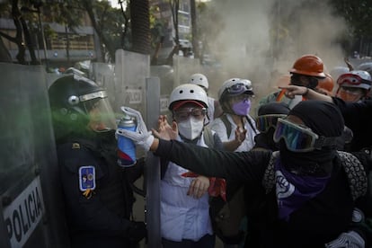 Una mujer del llamado "bloque negro" pinta los escudos de la policía con el color verde que se ha distinguido como símbolo del movimiento feminista en América.