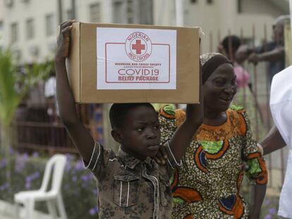Un niño y su madre en el suburbio de Makoko, en Lagos, transportan una caja con comida que han recibido de la Cruz Roja nigeriana el pasado domingo.