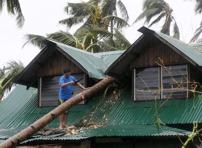 Un home intenta tallar un arbre caigut sobre la teulada d'una casa a Borongan.