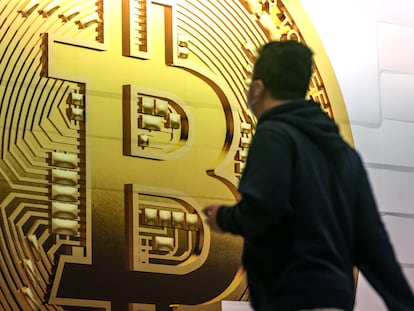 A pedestrian walks past an advertisement for the Bitcoin cryptocurrency.