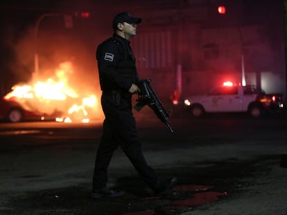 Un oficial de policía camina junto a un vehículo incendiado por miembros del Cártel Jalisco Nueva Generación, en Zapopan, Estado de Jalisco, el 9 de agosto de 2022.