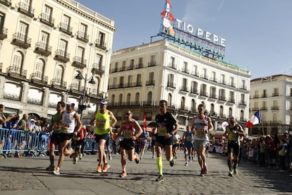 Varios corredores de la Maratón Popular de Madrid, pasan por delante de la nueva ubicación del cartel del "Tío Pepe" en la Plaza de Sol, de Madrid.