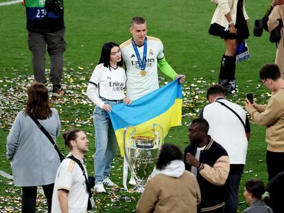 Lunin, junto a su novia, posa con la bandera de Ucrania y la copa de la Champions League que ha logrado con el Real Madrid.