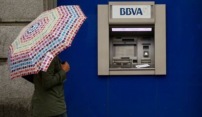 Una mujer cn un paraguas paseando delante de un cajero de BBVA