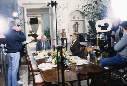 John Forsythe y Linda Evans en el comedor de 'Dinastía', donde se acumulan los símbolos de poder de la decoración Carrington: generosos buqués florales, 'boiseries' pintadas de blanco, ficus a tutiplén o jarrones chinos del tamaño de un niño de 12 años. |