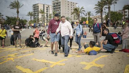 Dos hombres intentan pisar cruces amarillas con toallas en la playa de Mataró este domingo.