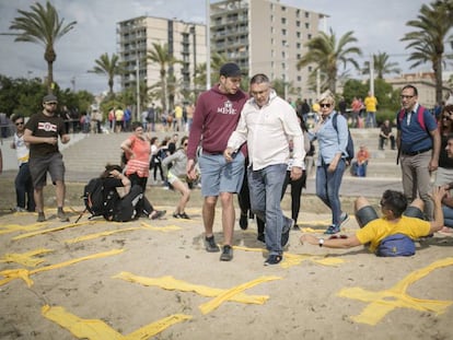 Dos hombres intentan pisar cruces amarillas con toallas en la playa de Mataró este domingo.