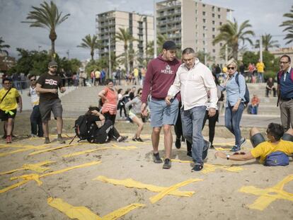 Dos hombres intentan pisar cruces amarillas con toallas en la playa de Mataró este domingo.