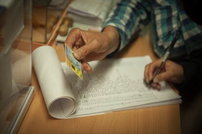 Un miembro de una mesa electoral comprueba el DNI de un votante, en el colegio Pare Poveda de Barcelona.