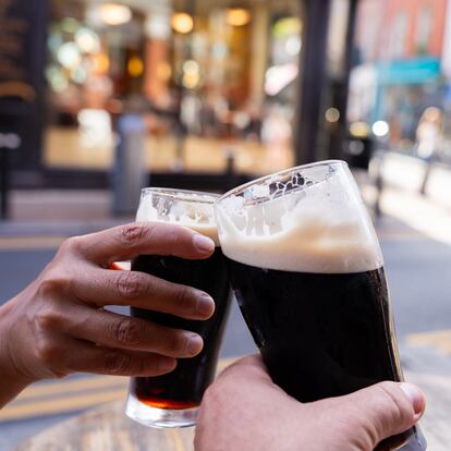 Close up of two hands holding two Guinness beers and toasting them in the center of Dublin on a beautiful autumn morning on the street