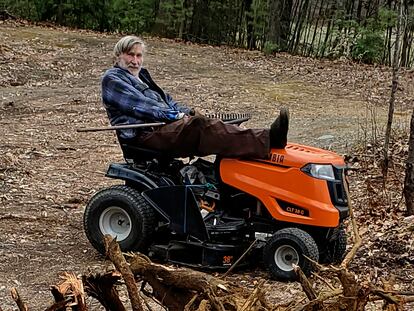 In this photo provided by Ed Smith, Geoffrey Holt rests his leg on top of his riding mower in Hinsdale, N.H., on April 4, 2020.