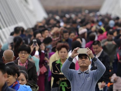 Un hombre toma una foto en el abarrotado puente de cristal de Zhangjiajie, China, un habitual destino tur&iacute;stico.
