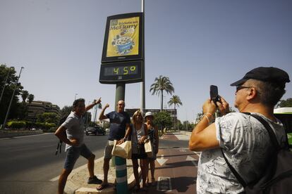 Unos turistas se fotografían en una calle de Córdoba debajo de un termómetro que marca 45 grados, este jueves.