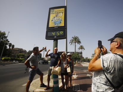 Unos turistas se fotografían en una calle de Córdoba debajo de un termómetro que marca 45 grados, este jueves.