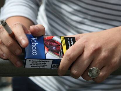 Un joven fumando con una cajetilla de tabaco en la mano