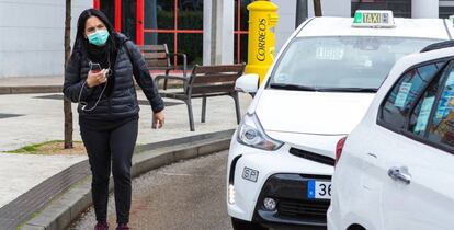 Una mujer camina por la calle junto a una parada de taxis en Madrid con una mascarilla.