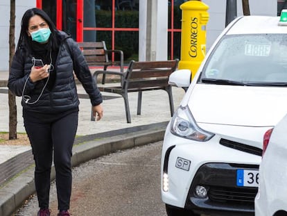 Una mujer camina por la calle junto a una parada de taxis en Madrid con una mascarilla.