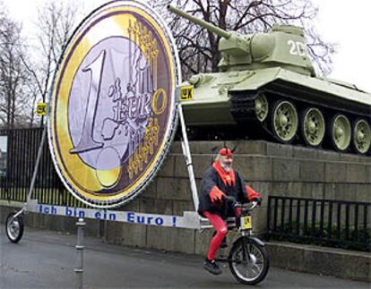 Un ciudadano, disfrazado de demonio, arrastra con su bicicleta una moneda para una campaña del euro en Berlín.