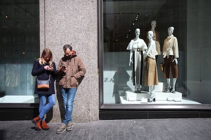 Una pareja consulta sus teléfonos móviles frente al escaparate de una tienda en el centro de Madrid.
