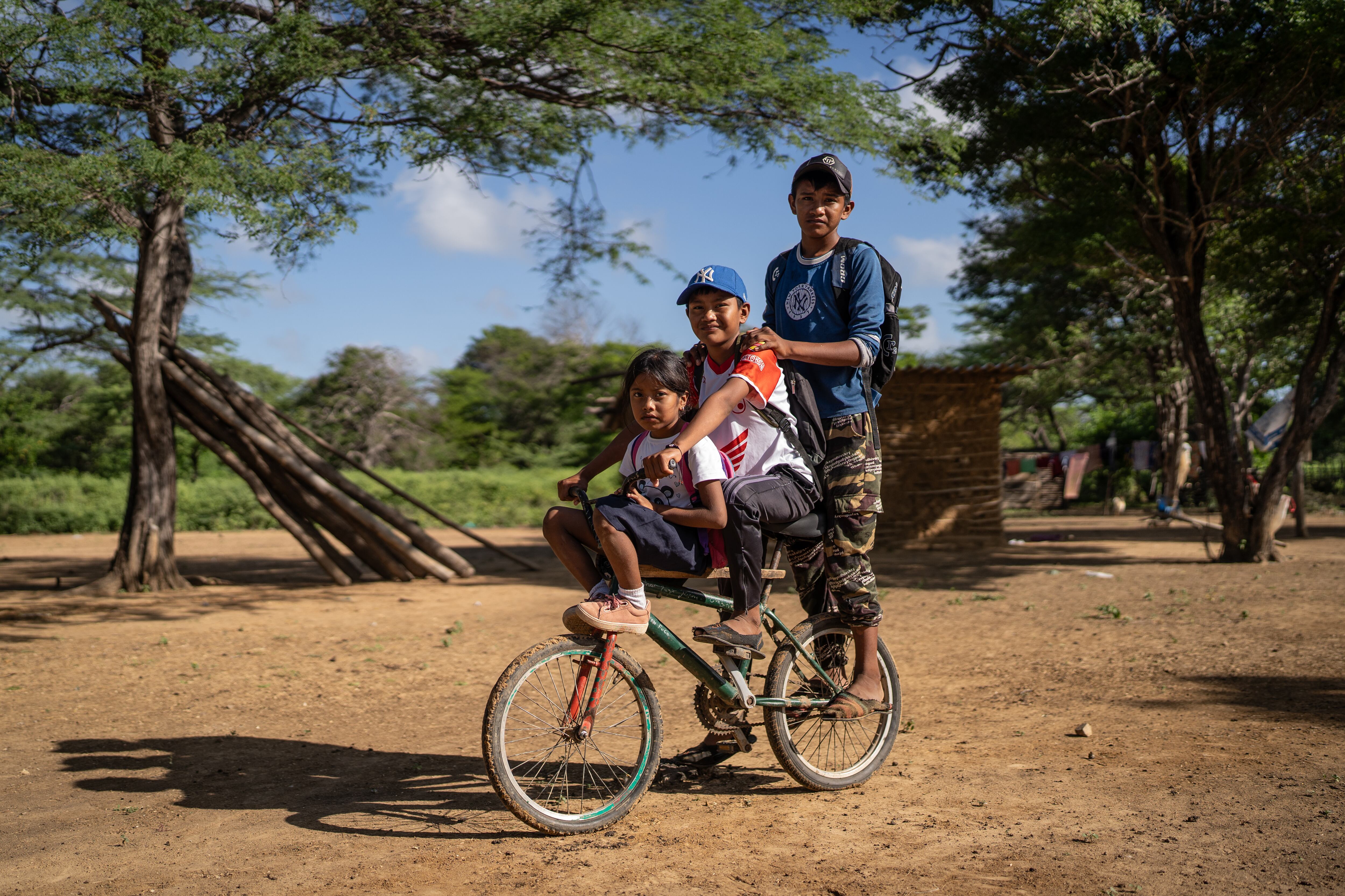 Kairun (7), Jimay (13) y Jasay (14) en la bicicleta en la que se transportan los tres para llegar a clases a la escuela Mulamana.